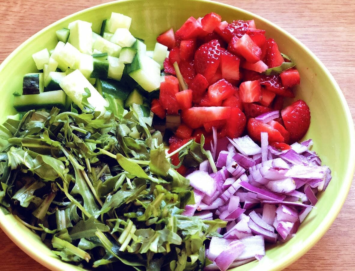Chopped strawberries, cucumbers, aragula leaves and onions in a bowl