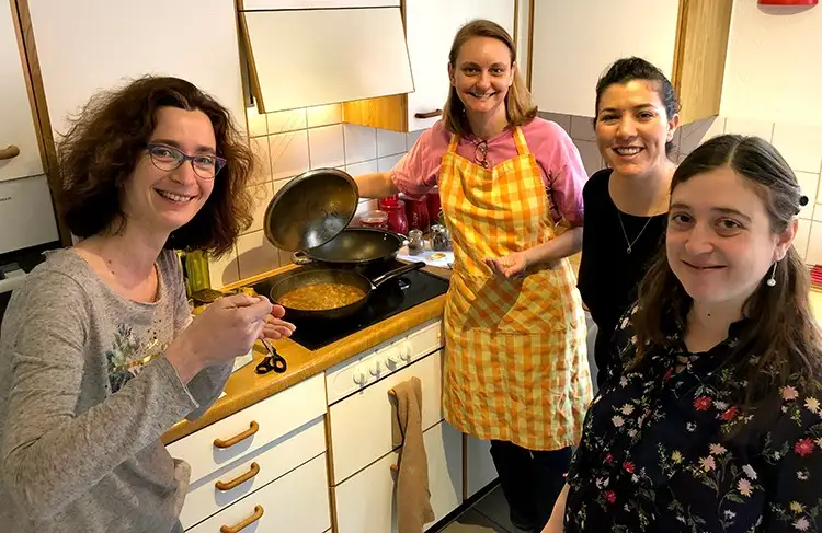 Ladies standing in a kitchen learning Indian cooking. 